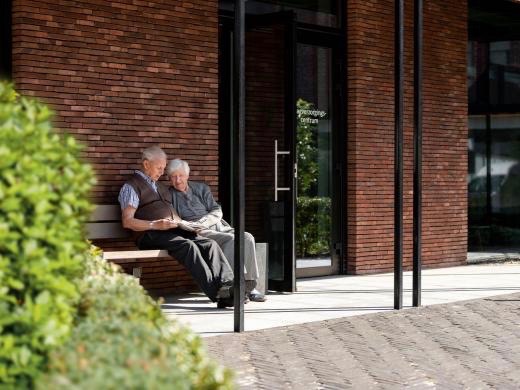 Ouder echtpaar in overleg op een bankje op het binnenplein van woonzorgcentrum de Refuge in Gent