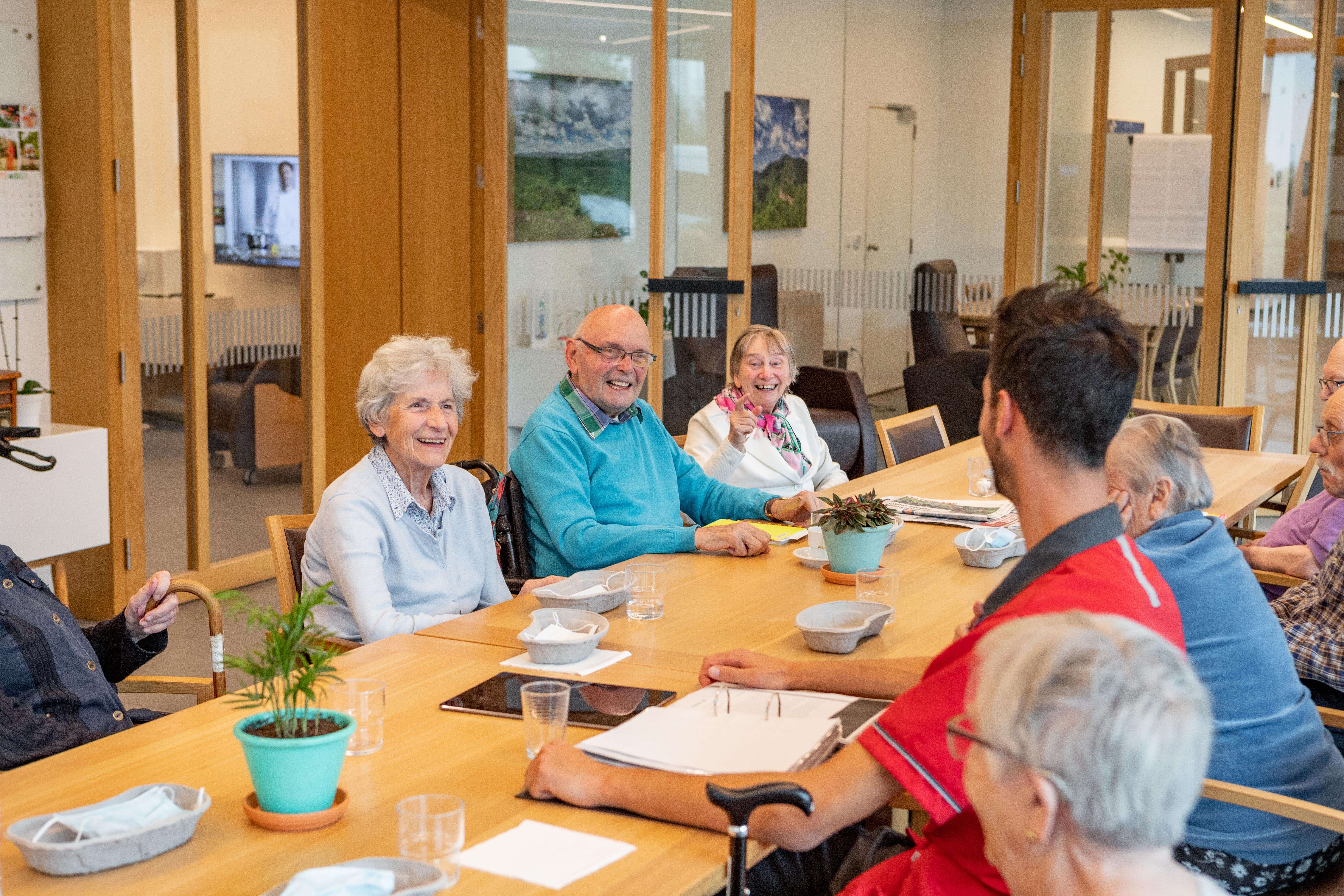 Oudere personen genieten van het sociale contact ana de grote tafel in het Dagverzorgingscentrum De Refuge in Gent