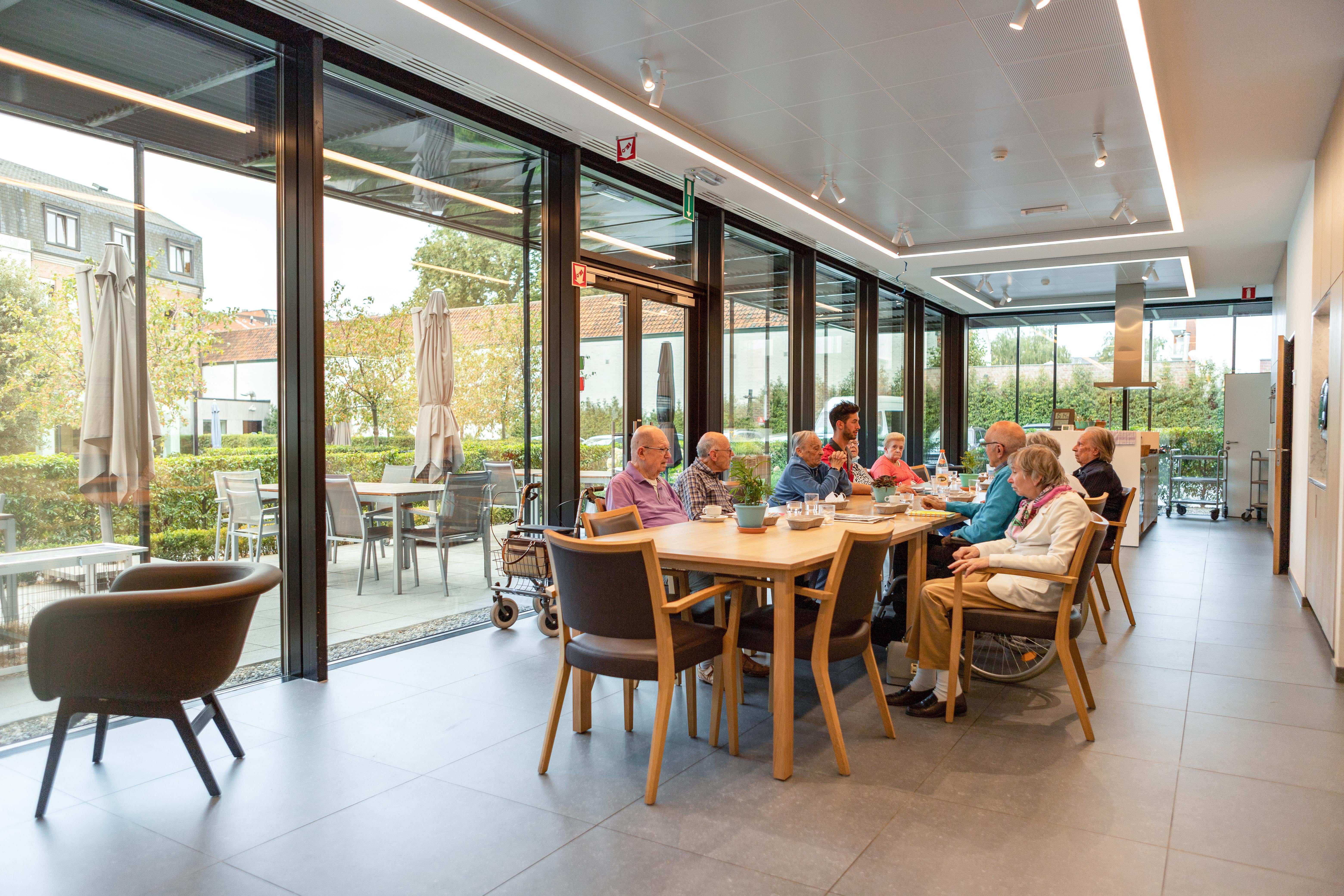 Oudere personen aan de grote tafel in het Dagverzorgingscenyrum De Refuge in Gent