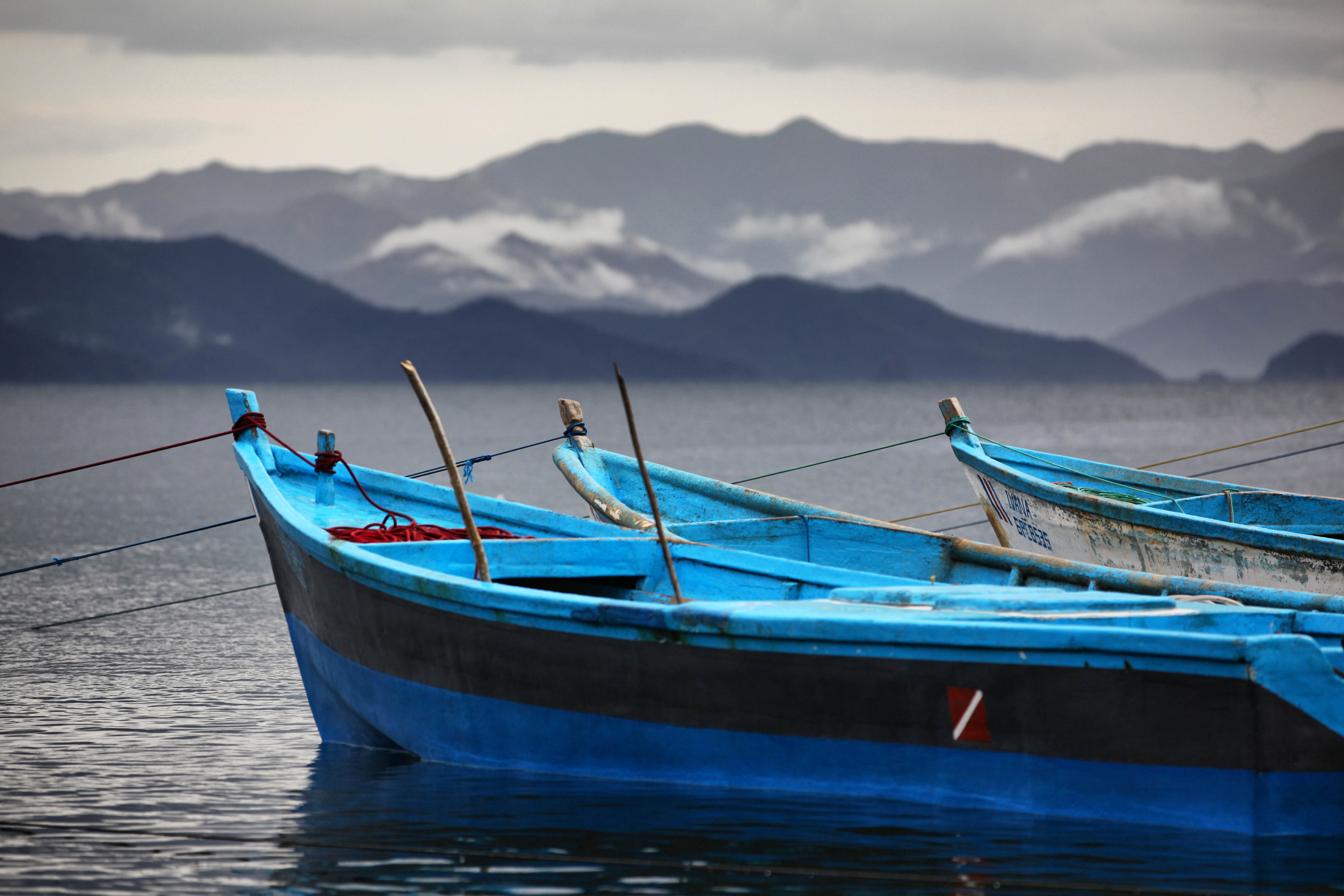 Blauw geschilderde boten op een rustig meer met mistige bergen op de achtergrond
