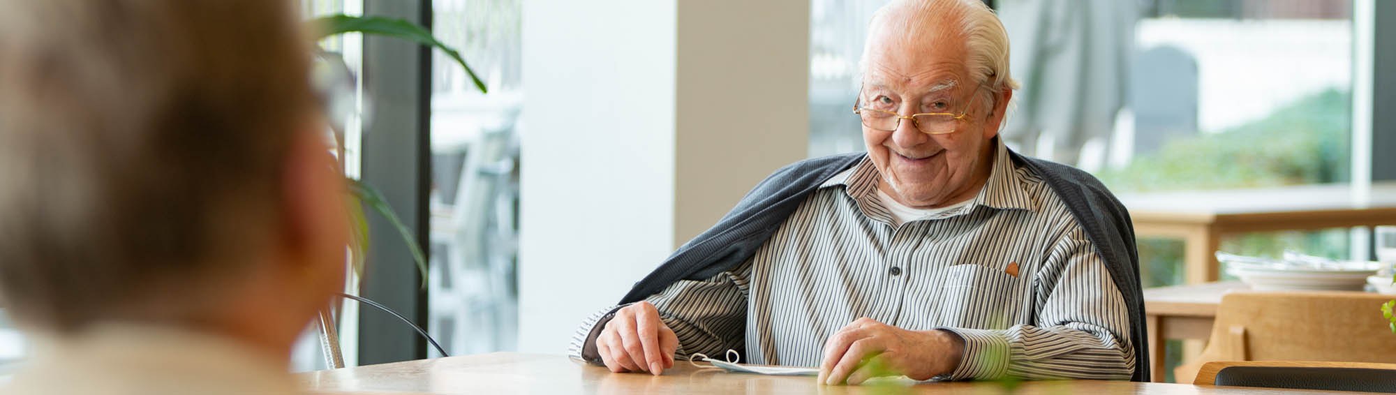 Glimlachende oudere man in het restaurant van de Refuge Gent leest de krant. 