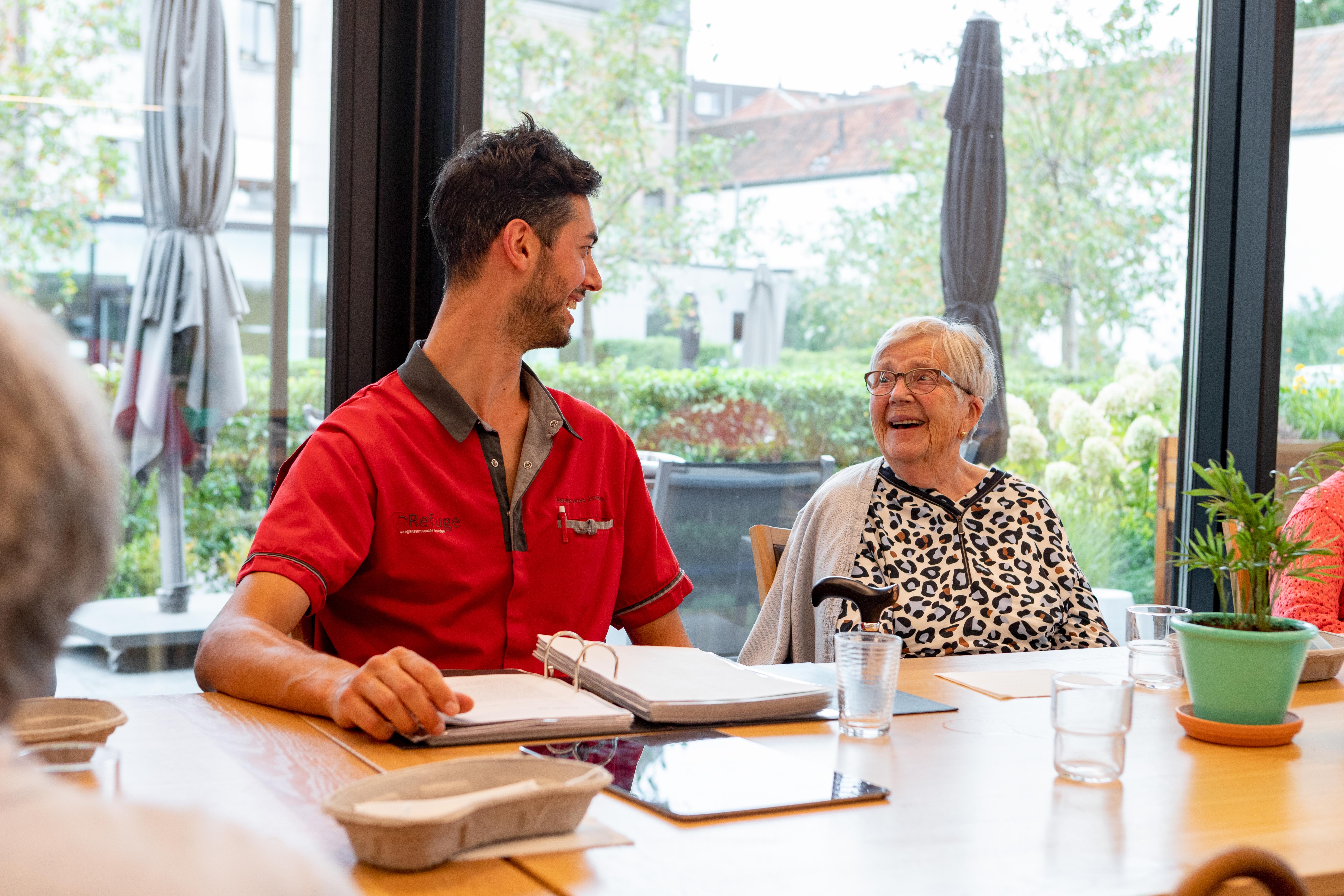 Lachende oudere en zorgkundigeaan de grote tafel in het Dagverzorgingscentrum De Refuge in Gent