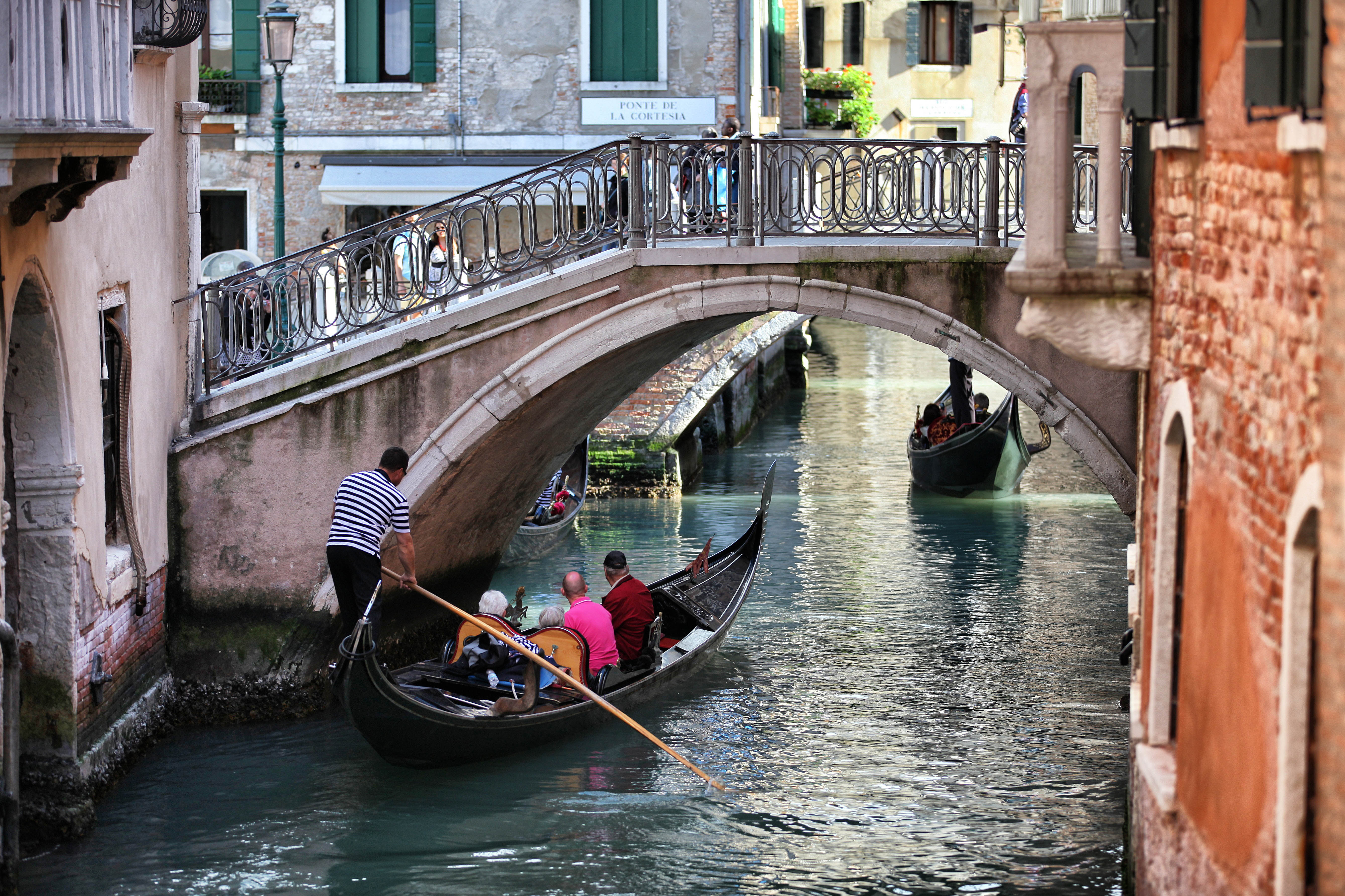 Gondelaar vaart met gondelen met toeristen onder een van de vele bruggen van Venetië
